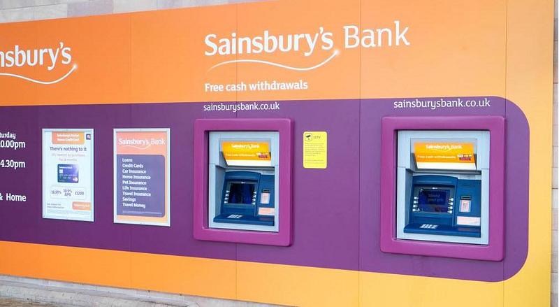 An outside wall with an orange mural and Sainsbury Bank ATMs