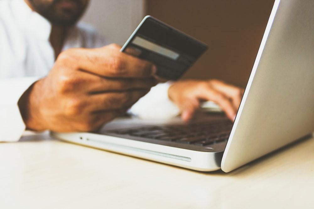 Man holding up bank card whilst typing on a laptop