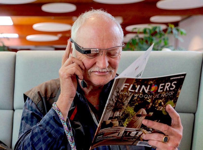 Older man using Envision Glasses to help read a magazine