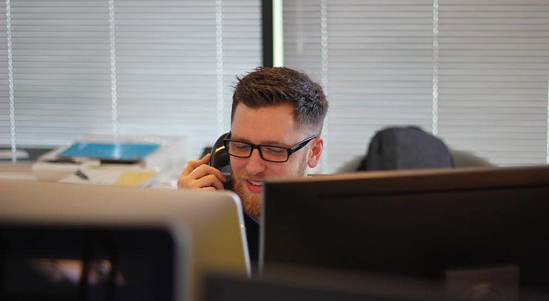 A man speaking on the phone behind two monitors