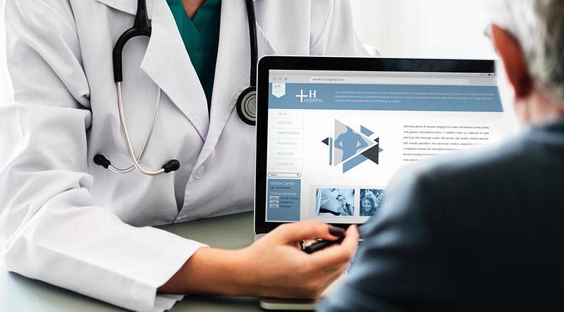 A doctor pointing at the information on a laptop screen in front of a patient